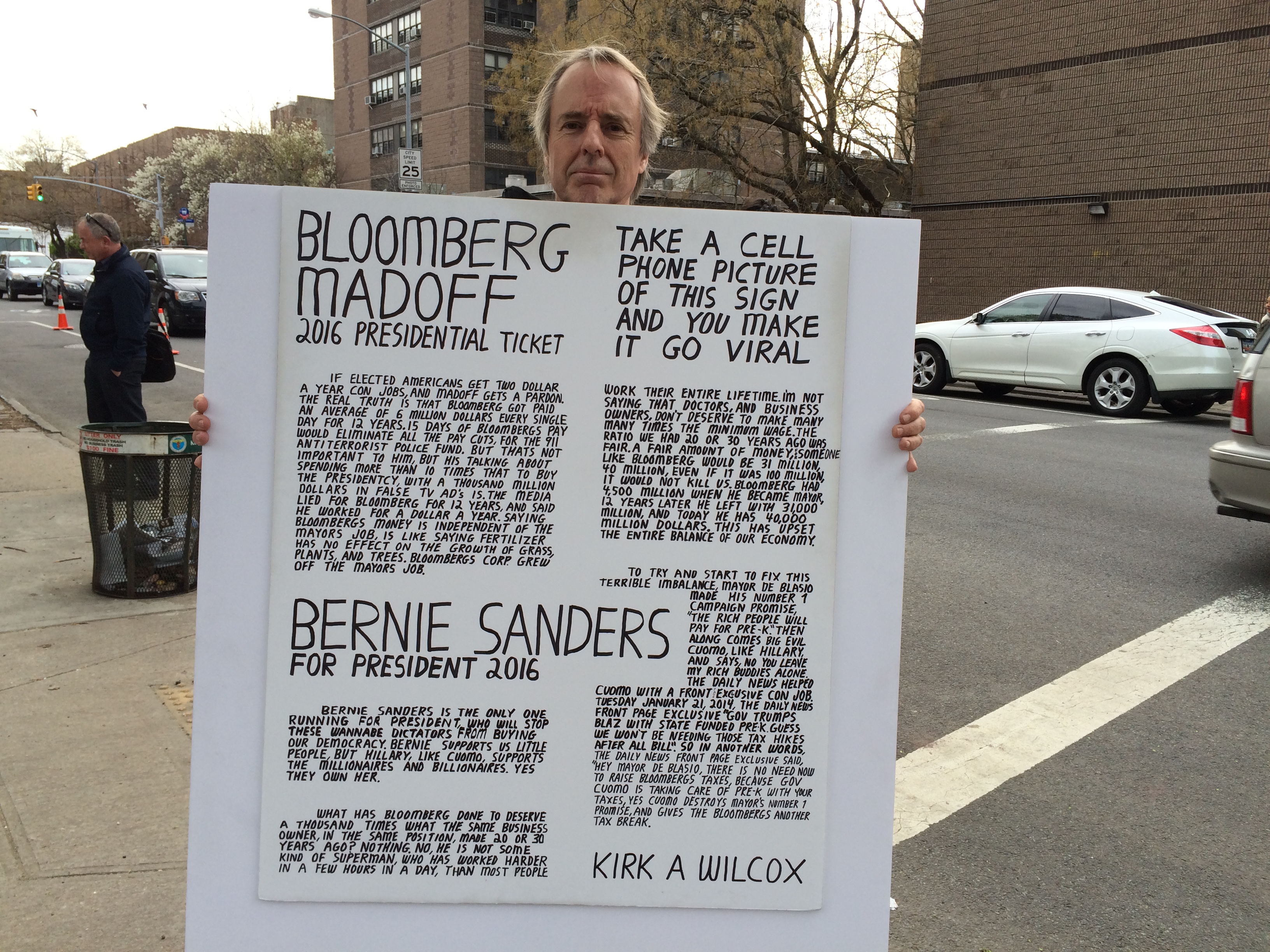 A Bernie Sanders supporters holding up a hand-written poster in form of a newspaper article - blasting Michael Bloomberg and Wall Street - Photo by Jacob Kornbluh